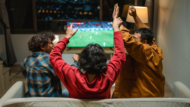 Three people cheering while watching football on TV