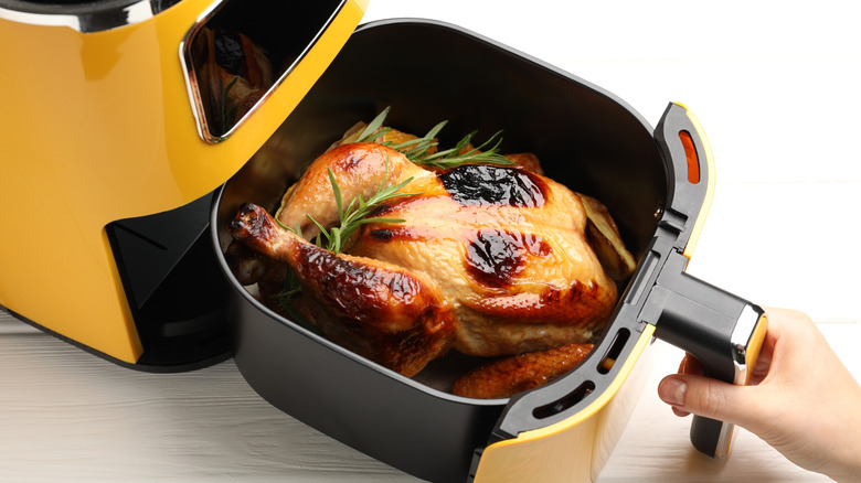 Hand opening an airfryer that contains a roast chicken