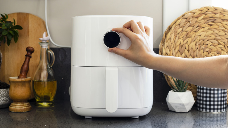 Hand turning the dial on an air fryer on a kitchen countertop