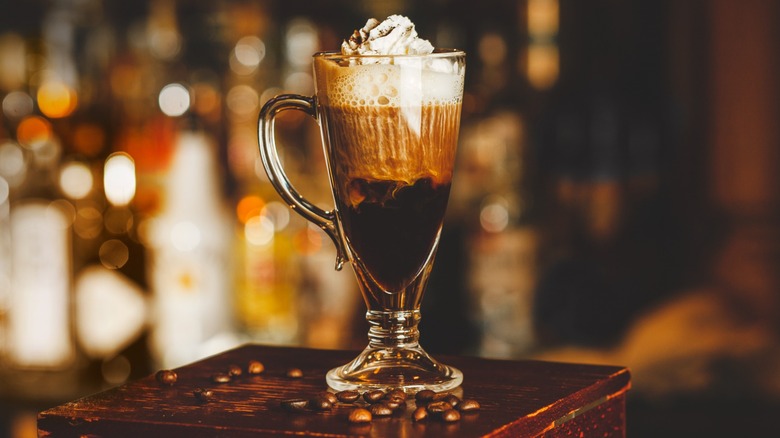 An Irish coffee cocktail on a table surrounded by coffee beans