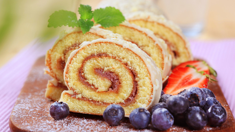 A sliced jelly roll cake on a cutting board with blueberries and strawberries