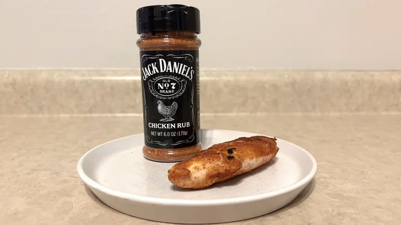 A bottle of Jack Daniel's chicken dry rub beside a white plate with a marinating piece of chicken