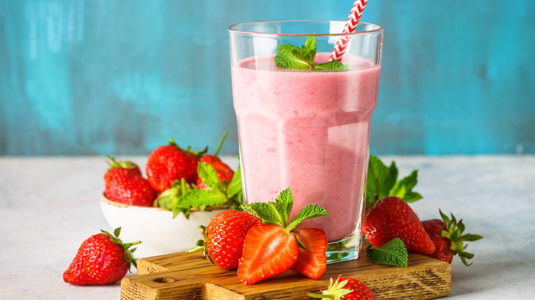 Strawberry smoothie in glass with striped straw surrounded by fresh strawberries