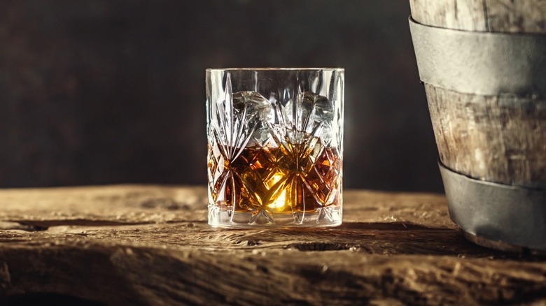 A glass of bourbon next to a barrel
