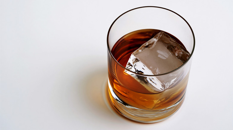 A high-angle view of a rocks glass of whiskey with a single large ice cube in it