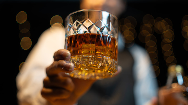 Handing hold rocks glass of whiskey