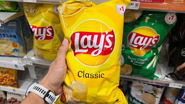 Someone holding out a classic bag of Lay's potato chips at the grocery store with the other chips behind it