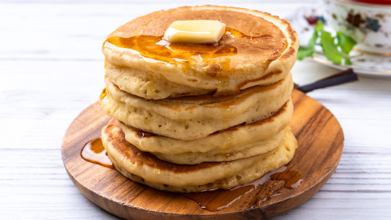 Stack of thick pancakes with butter and syrup on wooden board