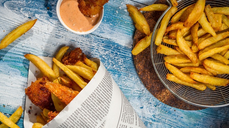 Fish and chips wrapped in newspaper next to bowl of fries and dipping sauce