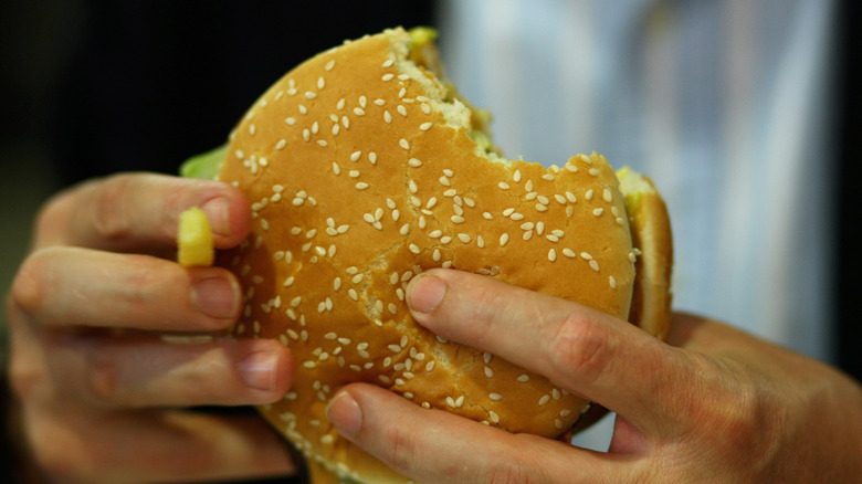 hands holding a burger with two bites taken out of it
