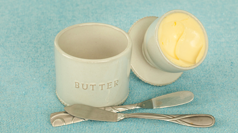 A butter crock alongside butter knives