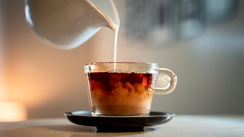 Pouring milk into a glass cup of black tea
