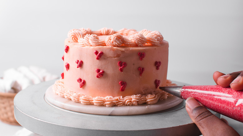 Hand piping hearts onto pink cake