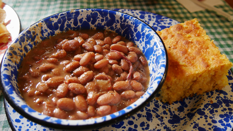 A blue and white bowl full of brown sauce and pinto beans next to a piece of golden cornbread