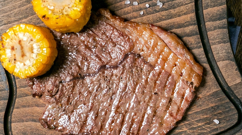 Grilled beef steak on a wooden board with roasted corn rounds