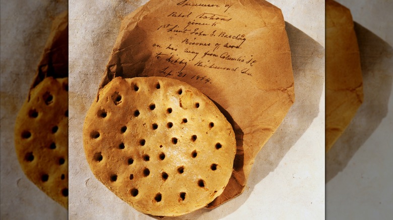 Around piece of hardtack with holes in it sitting on old, brown paper with writing