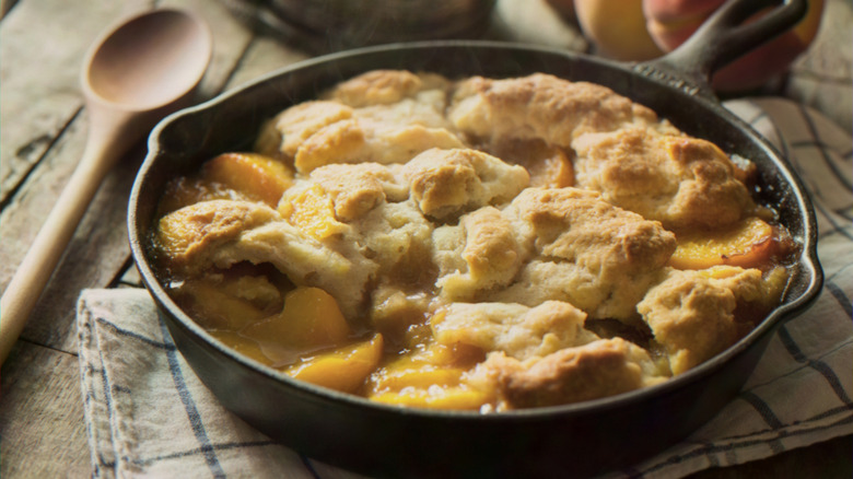 Peach cobbler in a cast iron frying pan with a golden biscuit crust on top