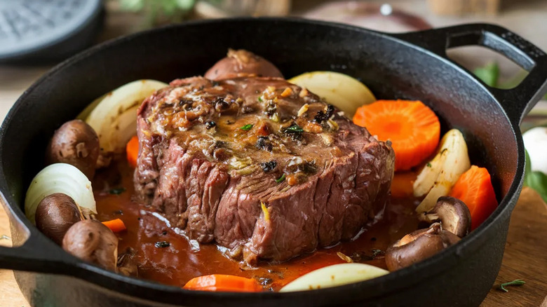 A beef roast in a cast iron pot with carrots, onions and mushrooms