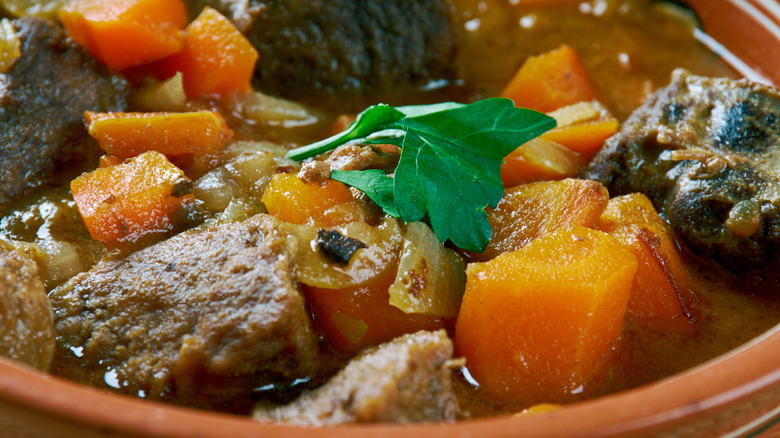 Close up on a bowl of son of a gun stew featuring big chunks of meat, carrot, onions, and a rich, brown gravy