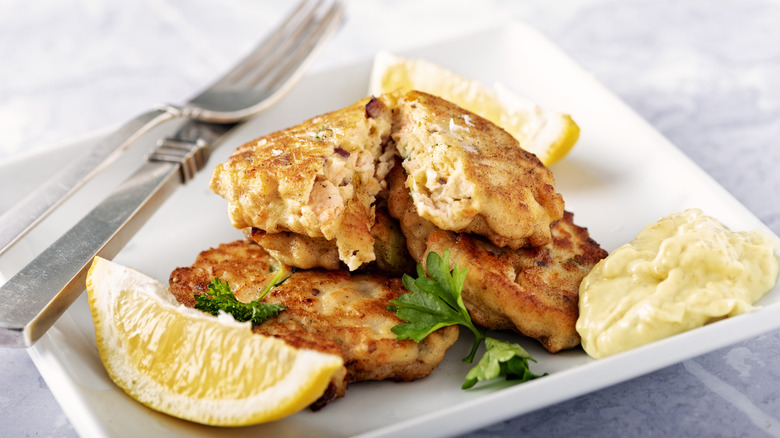 Salmon cakes with lemon slices and yellow sauce on white plate