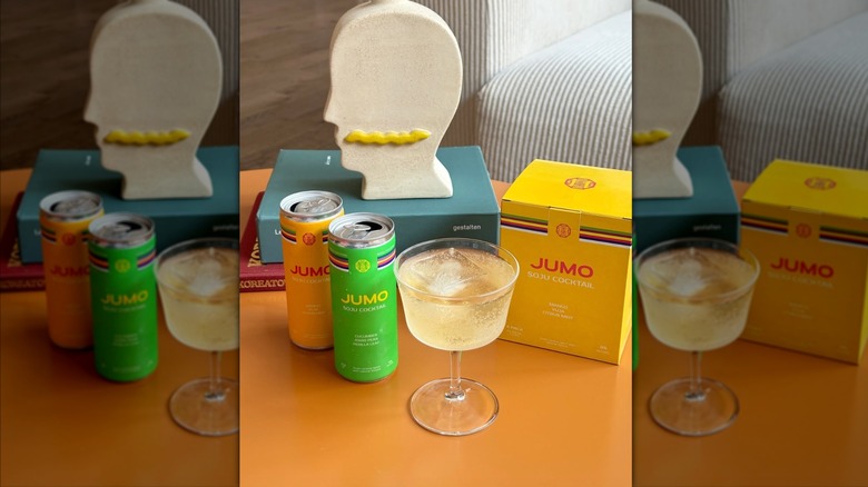 Two Jumo canned cocktails and coupe glass on orange table
