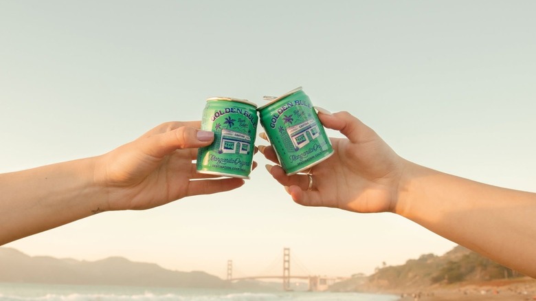 Two hands cheersing with cans of Golden Rule cocktails