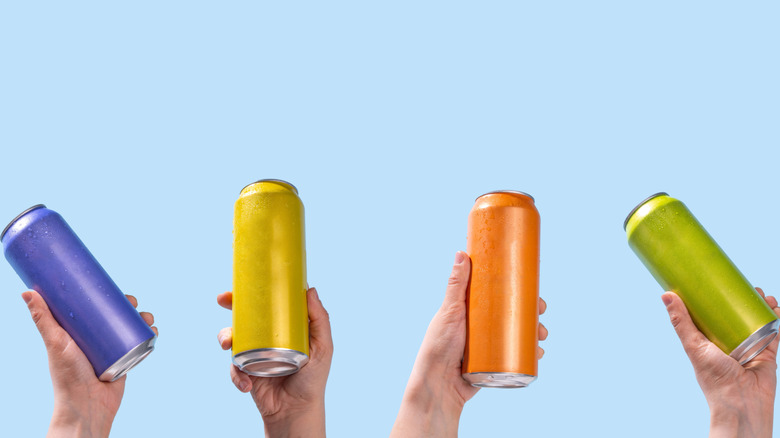Hands holding colorful canned cocktails against light blue background