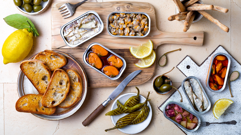A variety of tinned fish spread out along with bread, lemons, peppers and other accoutrements