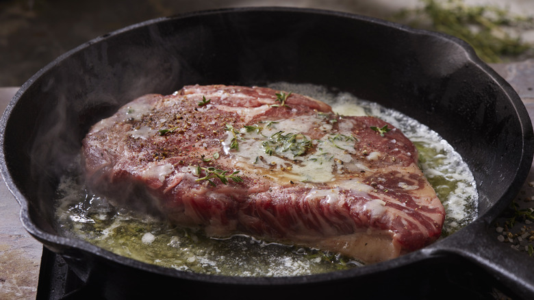 ribeye steak cooking in pan