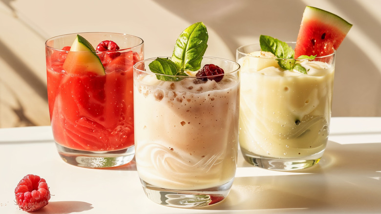 3 smoothies in glasses topped with fruit and herbs
