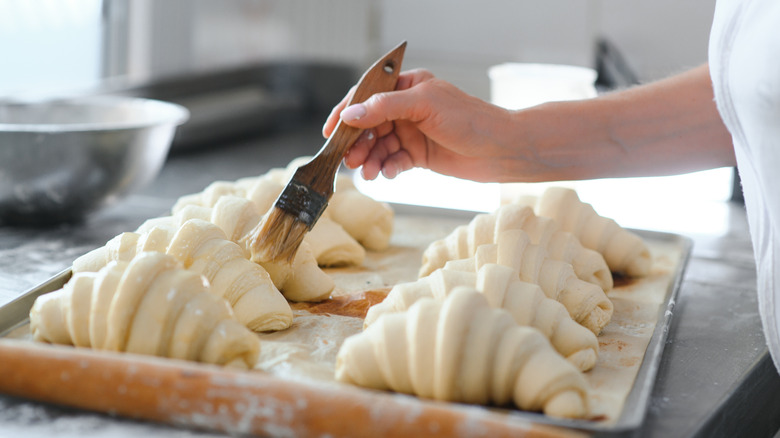chef washing a pan of uncooked croissants with a small brush