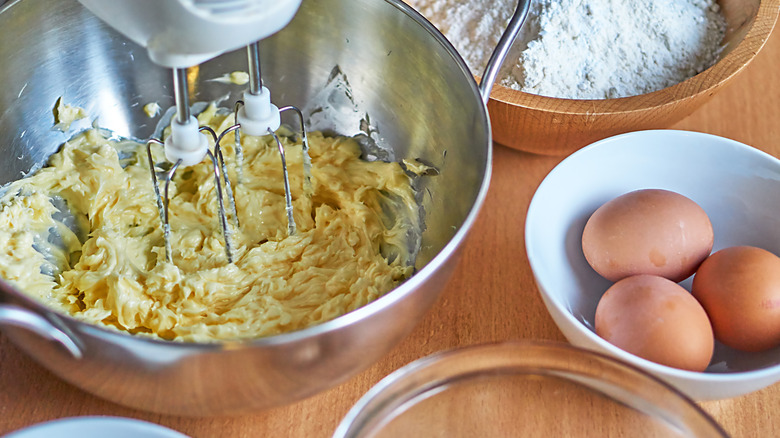 eletric mixer in bowl of creamed butter beside bowls of eggs and flour