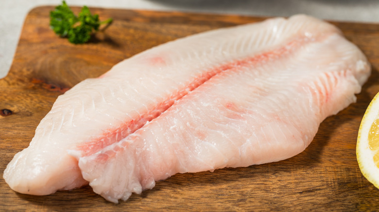 A raw catfish fillet on a wooden cutting board