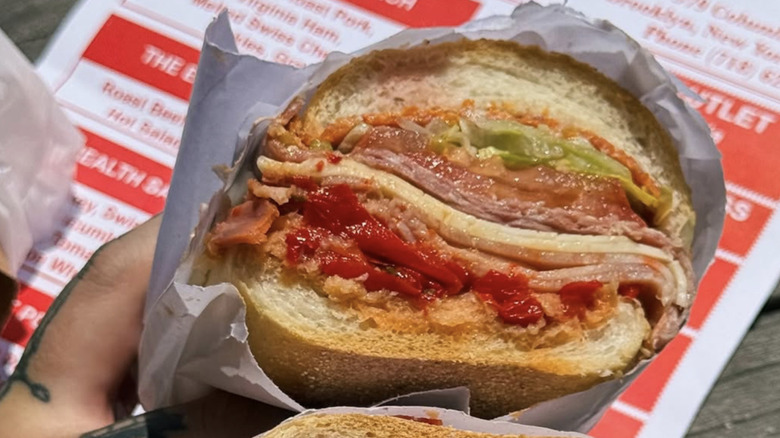 hand holding sliced sub sandwich wrapped in paper