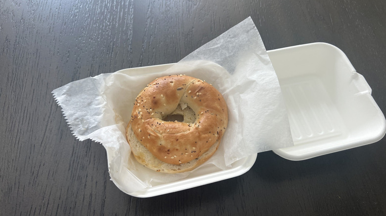 an everything bagel on a piece of deli paper inside of an open clamshell to-go container