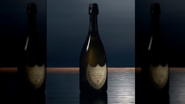 A single bottle of Dom Perignon seemingly floats on the water of an infinity pool with a dark sky behind
