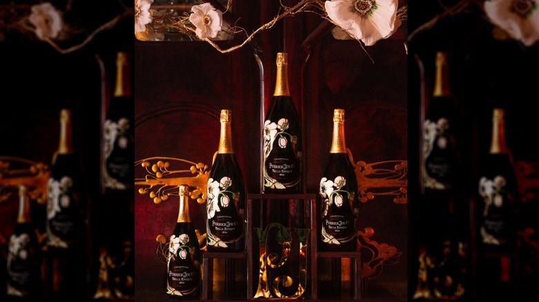 Several bottles of floral decorated Perrier-Jouët Champagne bottles are in front of a rich, artistic, floral background