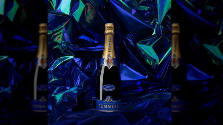 A textured iridescent blue cellophane background showcases a blue labeled bottle of Pommery Champagne.