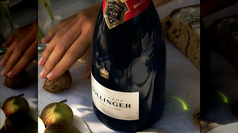 A bottle of Bollinger special cuvee with a hand in the back surrounded by walnuts and figs