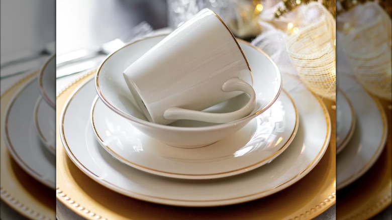 A stack of three white plates and a mug with golden rim