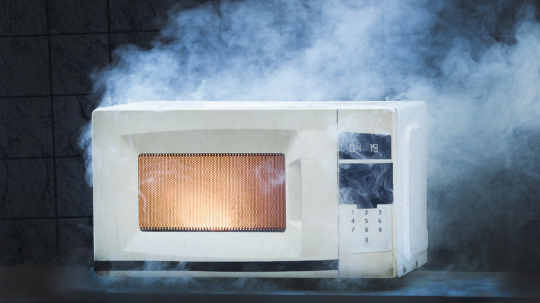 Photo of a smoking white microwave with a flame visible inside