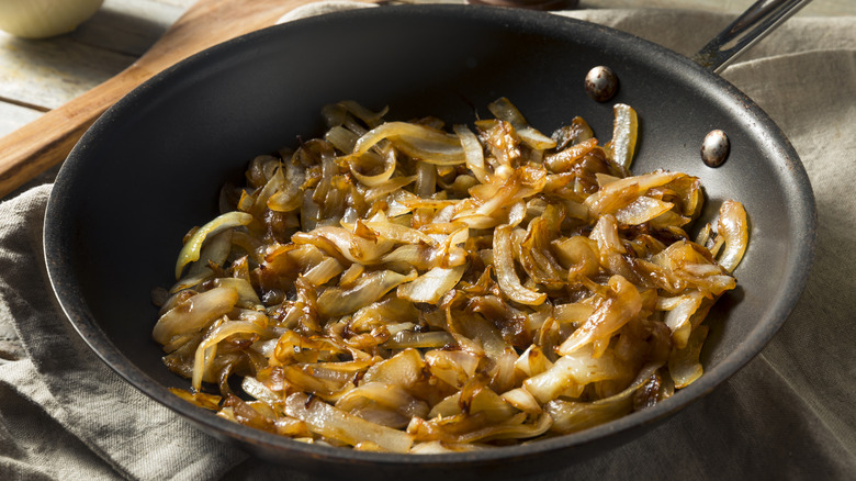 A frying pan of caramelized onions rests on a kitchen towel