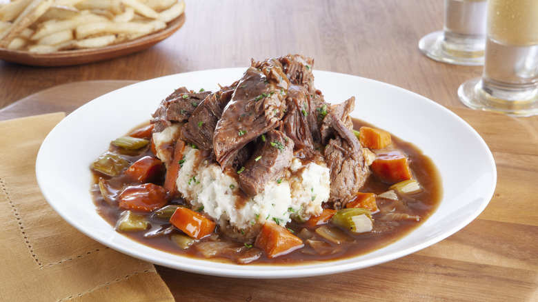 A plate of pot roast on top of mashed potatoes sitting on a wooden table