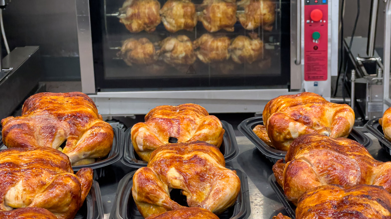 Black trays of rotisserie chickens being prepared in store