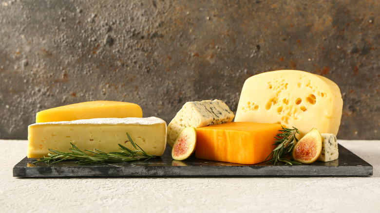 Several varieties of cheese on a board with figs and rosemary