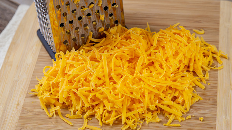 A pile of shredded cheddar cheese next to grater