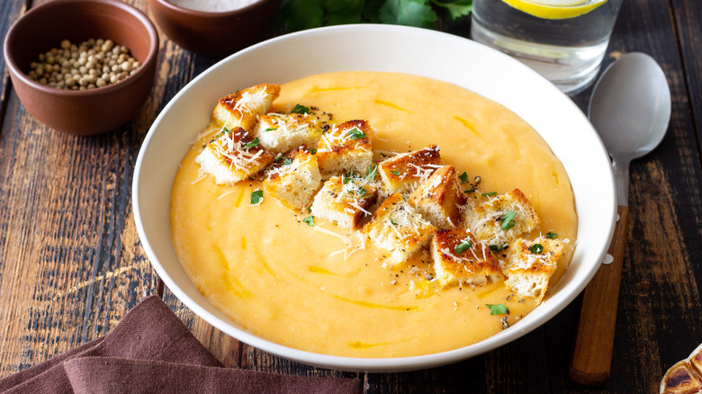 a bowl of cheese soup topped with croutons on a wooden table