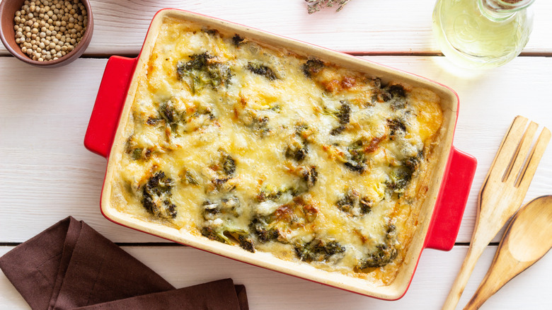 a pan of cheesy broccoli casserole on a table beside spices and utensils