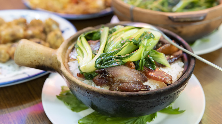 Cantonese clay pot rice with bok choy on top and other dishes in the background.