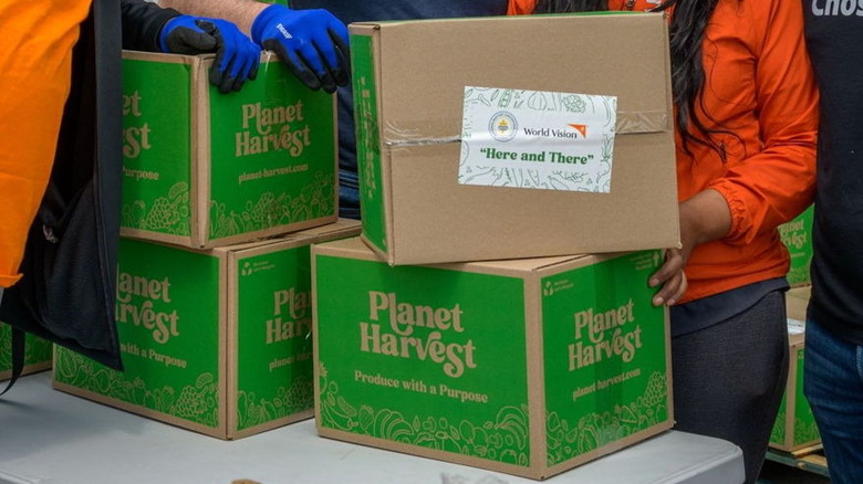 carboard boxes on a table labeled with the Planet Harvest logo and people in the background
